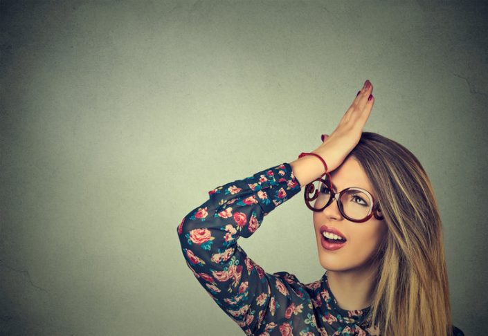 silly young woman, slapping hand on head having duh moment. Regrets wrong doing